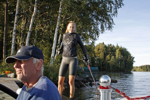 Jouko Lammi ajaa moottorivenettä tyttärensä suorituksen aikana. Mette Lammi kiskoo suksen jalkaansa saippuan avulla. Kuva: Ida Nieminen